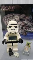 Large Stormtrooper figure with digital clock and small Darth Vader and Millennium Falcon miniatures in front, Millennium Falcon 3D puzzle box in background