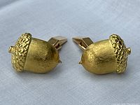 Pair of acorn cufflinks displayed side by side on fabric