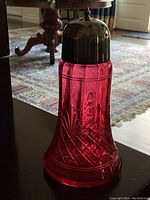 Front and side view of antique cranberry glass sugar shaker with silver plated lid on a dark surface showing etched design and finial detail