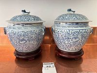 Two blue and white porcelain ginger jars with lids and foo dog finials on wood stands