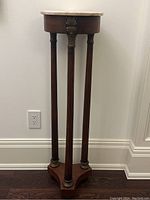 Front view of full pedestal showing round marble top, three fluted columns, and tripod base