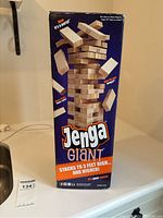 Front view of the Giant Jenga box showing the product name, visuals of the wooden blocks in play, and highlighting that the set stacks to 3 feet high and higher.