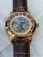 Watch face view showing skeleton dial, rose gold tone case, blue hands and Arabic numeral markers