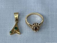 Ring setting and emerald pendant displayed side by side on fabric background