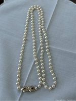 Full 32-inch single-strand pearl necklace with horseshoe-shaped gold-tone clasp laid flat
