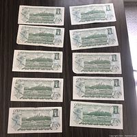 Top and bottom side of 11 and 10 $1 Canadian bills arranged in two groups on a wooden surface