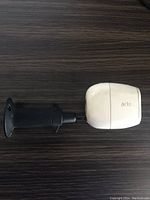 Side-profile photo of white Arlo security camera attached to black mounting bracket on wood surface.