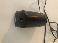 Front view of black cylindrical X-ACTO electric pencil sharpener with pencil insertion hole and power cord visible.