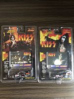 Photo showing the front packaging of two Johnny Lightning KISS cars featuring Peter Criss and Gene Simmons in original sealed blister packs.