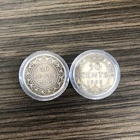 Two silver half dollar coins from Newfoundland dated 1899 and 1909, showing the reverse sides with denomination and designs inside Airtite capsules on a wooden surface.