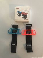 Two Nintendo Switch Dance armbands; blue and pink with black straps, alongside the product box showing usage for Switch Dance game.