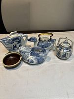 Five Asian blue and white porcelain items arranged on a white cloth, showing various shapes and decorations including teapots and a dish.
