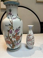 Two Chinese porcelain vases shown side by side on a table, showcasing their size difference and detailed painted decorations with birds and flowers.
