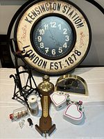 View of full lot showing round wall clock, wooden barometer, porcelain heart-shaped boxes, brass desk clock, porcelain vase, miniature bicycle figurine, and glass vial.
