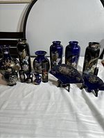 Multiple vintage Japanese porcelain items including vases, pitchers, and decorative pieces on white cloth against dark furniture background.