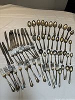 Full collection of silver plate flatware laid out on white cloth showing knives, forks, and spoons of various sizes.