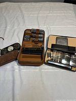 Photo showing a vintage brown leather man shave kit with various small glass jars, metal containers, and a mirror inside the case, alongside another similar leather shave kit with glass jars and metal containers.