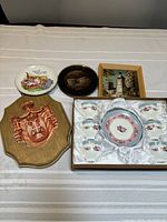 Collection of porcelain tea set in box, two decorative plates, and two wooden plaques displayed on a table.
