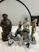 Photo showing the large bronze-tone sailor statue, the three sailor group figurine, and three small blue and white porcelain dancing girl figurines arranged in front of a circular mirror.