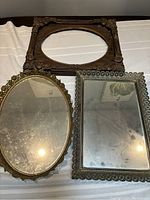 Three frames: large carved wooden oval frame, silver-plated rectangular frame, and ornate oval mirrored frame with visible mirror spotting.
