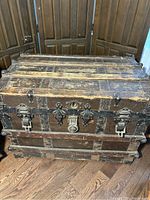 Front view of the large wooden storage trunk showing the worn wood panels, metal reinforcements, latches, lock, and hardware details.