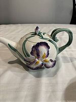 Side view of the teapot showing the floral design on the body, the curved green handle, and spout.