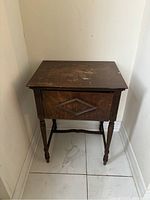 Closed view of the antique wooden sewing table with turned legs and a geometric design on the front panel.