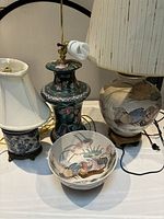 Photo showing three vintage Asian-style table lamps and one decorative ceramic bowl on a table, lamps untested, showcasing variety and condition.