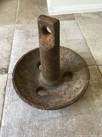 Photo of a heavily rusted metal boat anchor with circular base and upright shank showing wear and patina.