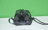 Back view of black compact binoculars showing lens caps and neck strap attached, resting on black zippered carrying case.