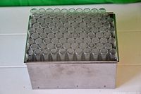 Rectangular metal box containing 94 clear glass vials arranged in rows, viewed from above.