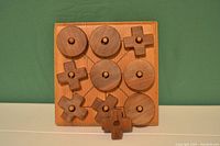 Wooden hand-crafted X's and O's game board with large X and O pieces placed on the board. Board is a 3x3 grid, 7.5 inches square, natural wood color.
