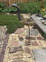 Heron yard art sculpture displayed on stone and gravel garden pathway showing layered feather details and overall shape.