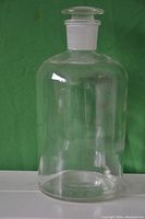 Clear glass laboratory storage jar with matching glass stopper shown against a green background.