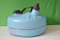 Side view of blue metal oil can showing dents, two screw caps on top, and rusted metal strap handle across the lid.