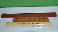 Four rulers laid out including the Rabone folding ruler, two Swift Feeds branded rulers, and one McLarens Limited Invincible Food Products ruler