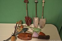 Image of vintage shoe trees and shapers laid out showing metal spring action with various colored caps and aluminum toe forms, some with perforated plates and leather heel supports.