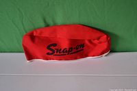 Red Snap-On branded welder's or mechanic's cap, laid flat on a green background showing the logo clearly