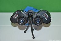 Front view of black Tasco 7x50 binoculars resting on a tripod, showing fully coated lenses and model branding.