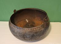 Side view of round metal bowl with rivets and handle showing internal wear and rust spots.