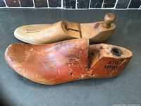 Two vintage wooden shoe forms, one natural wood and one reddish-brown with army markings, hinged and used