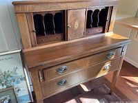 Full closed view of antique wood secretary desk showing laminate top, wooden lower drawers with metal handles, inlay on center cabinet door, and detailed cubby compartments.