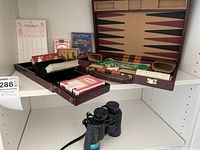 Overall view of opened backgammon board with cards and Minolta binoculars displayed.
