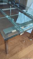 Corner view of clear glass tabletop and chrome finish metal frame and square leg