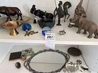 Shelf display of various figurines including brass dog, horse, two bowls, blue glass sphere and pewter framed mirror with small decorative items