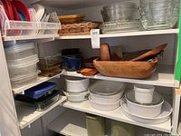 Overview of kitchen cabinet shelf showing assortment of plastic food storage containers, glass bowls, ceramic casserole dishes, wooden salad bowls and servers.