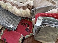 Overview of the linens showing crochet throw blanked, folded bed sheets in beige, grey and red, and woven rugs and place mats with various patterns