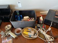 Image showing assorted office supplies including tape dispensers, cordless phone, glue bottle, organizer bins, cables, and paper clips arranged on a wooden surface