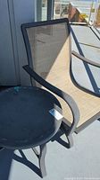 Side view of patio chair and circular side table on balcony showing weathered condition and dust.