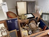 Collection of various small photo frames in wood, resin, and metal displayed on shelf and in box